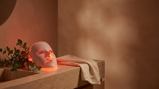 Red light therapy mask glowing softly on a stone vanity in a warm, spa-like setting