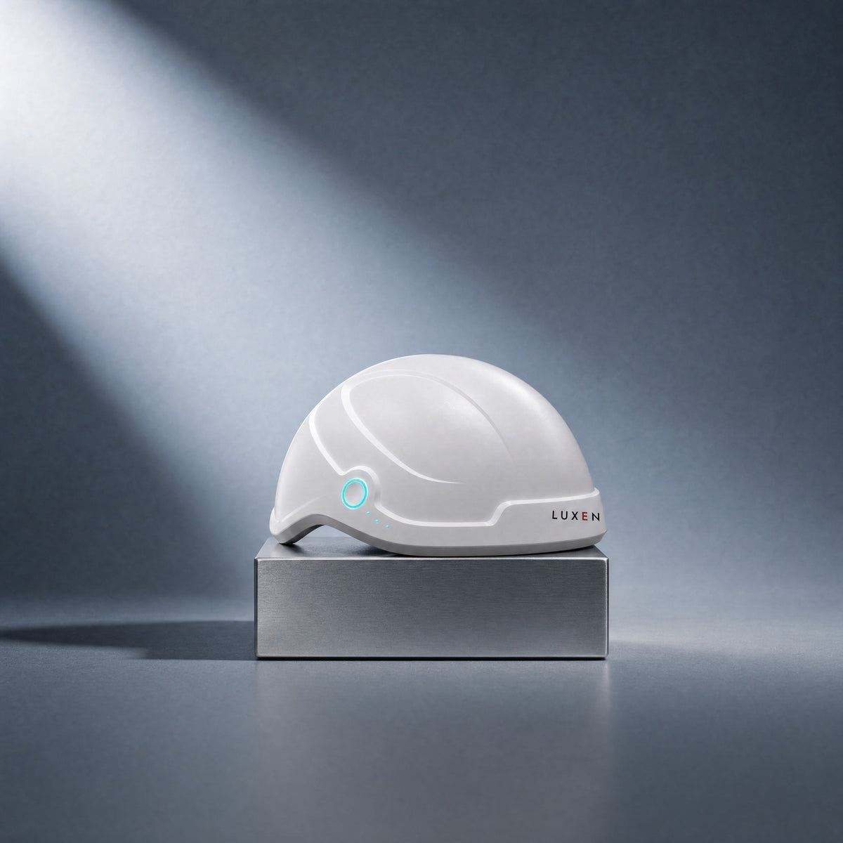 The white Luxen Laser Cap on a brushed steel block in soft studio light